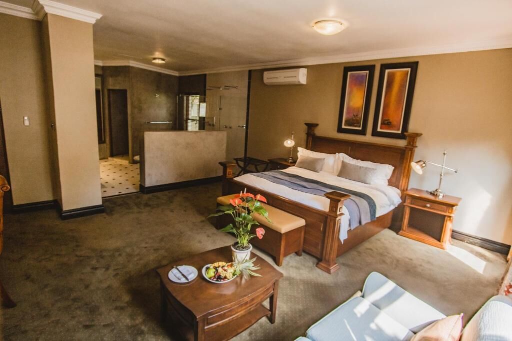 Quarto de hotel com cama, escrivaninha, cadeira, mesa pequena com um vaso de flores e janela com cortinas.