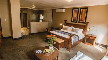 Quarto de hotel com cama, escrivaninha, cadeira, mesa pequena com um vaso de flores e janela com cortinas.