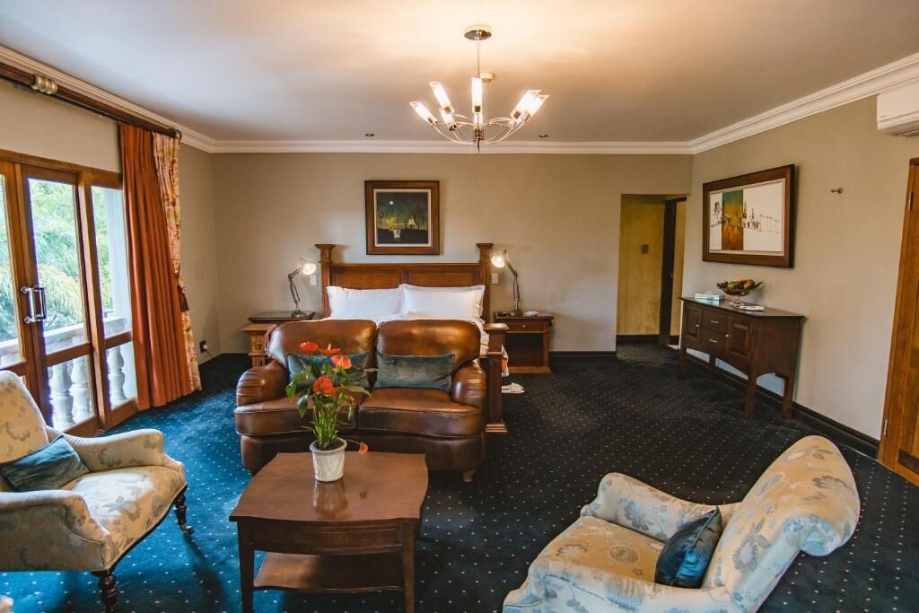 A hotel room with a large bed, two armchairs, a sofa, a small table with a vase of flowers, and a chandelier.