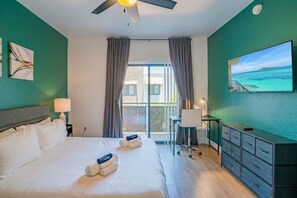 A hotel room with a bed, a desk, a chair, a TV, and a balcony with curtains. - Stadium-Adjacent | Pool, Balcony, Parking, Hot Tub (Glendale)