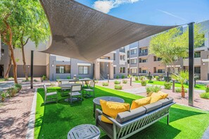 An outdoor patio with a table, chairs, and a sofa under a shade sail.