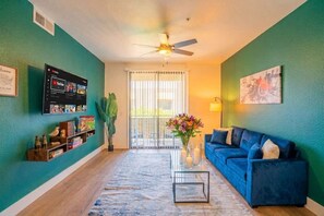 Un salon avec un canapé bleu, une table basse, une bibliothèque et un ventilateur de plafond.