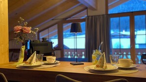 Un comedor con vigas de madera, una mesa preparada para dos personas y vistas a un paisaje nevado a través de grandes ventanales.