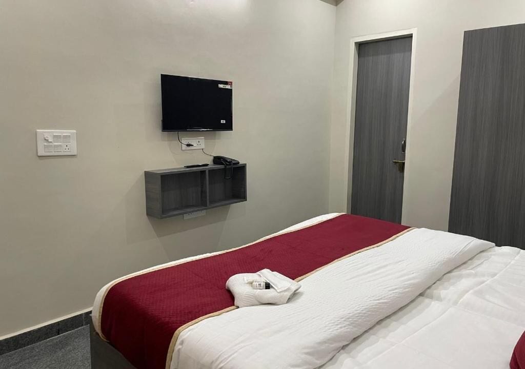 A hotel room with a bed, a television mounted on the wall, a door, and a small shelf.