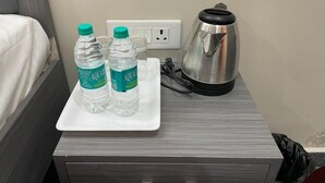 Une chambre d’hôtel avec un lit, une petite table blanche sur laquelle sont posées deux bouteilles d’eau Aquafina, une bouilloire et une prise électrique.