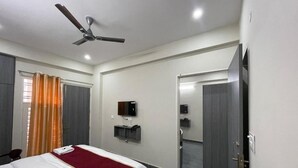 Une chambre d’hôtel avec un lit, un ventilateur de plafond, une télévision et une salle de bain visible à travers une porte ouverte.