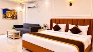 A hotel room with a large bed, a sofa, a small table, and a wall-mounted air conditioner. - Ravira Resort (Sitapur)