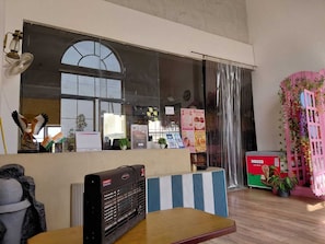 Una habitación con un ventanal grande, un radiador, una mesa con una radio y una estructura decorativa rosa con plantas.
