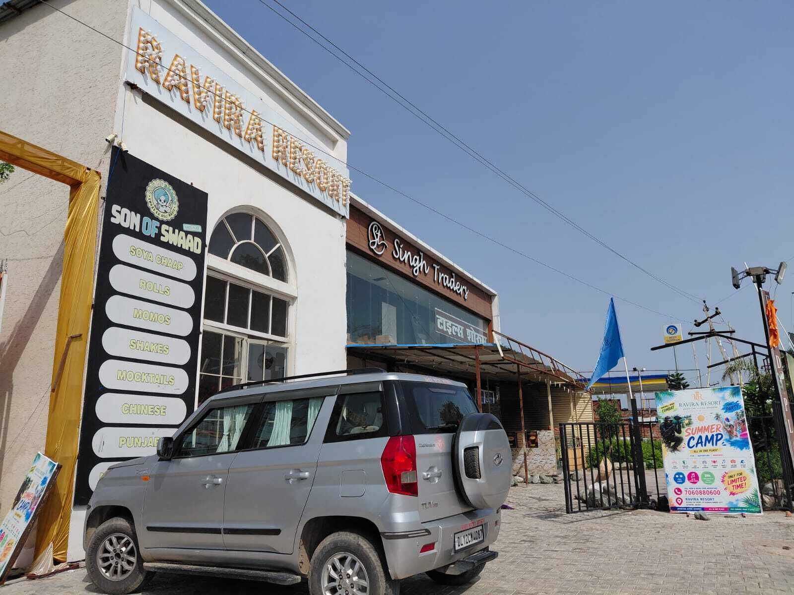 A building with a sign for 'Ravindra Traders' and a signboard listing various food items like Soya Chaap, Rolls, Momos, Shakes, Mocktails, Chinese, and Punjabi.