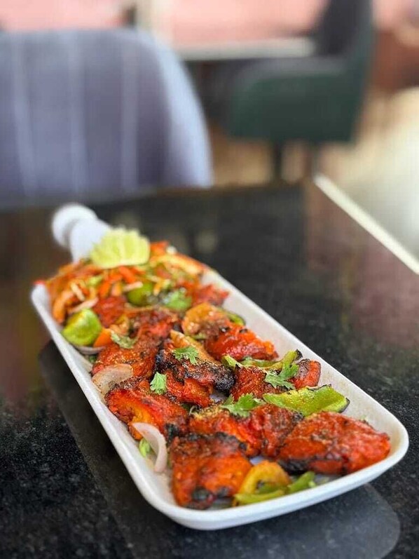 A rectangular white dish with grilled meat, vegetables, and a garnish on a dark surface. - Ravira Resort (Sitapur)