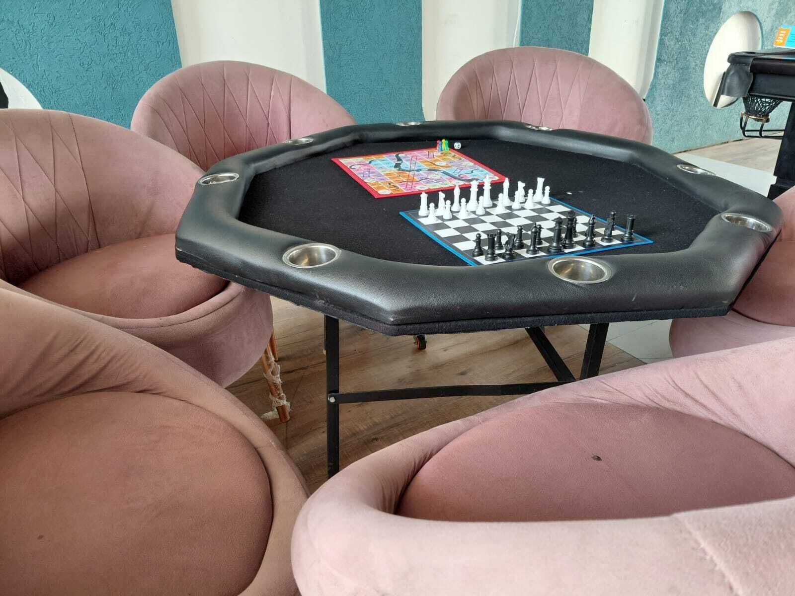 Une table hexagonale sur laquelle on peut jouer aux échecs et au Scrabble, entourée de chaises roses.
