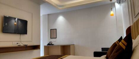 A modern hotel room with a large bed, a flat-screen TV mounted on the wall, a desk, and a bedside table.