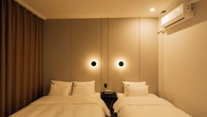 Une chambre d’hôtel avec deux lits, une table de chevet, un appareil de climatisation et un miroir avec un éclairage mural.