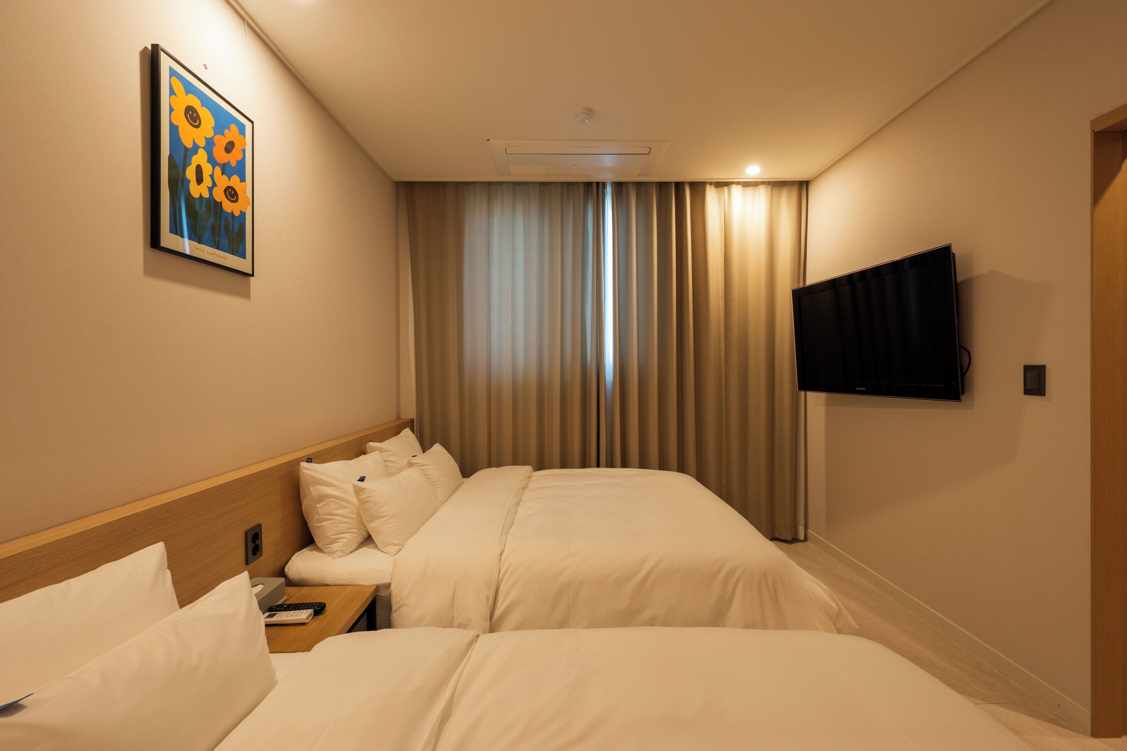 Habitación de hotel con dos camas, un televisor, un cuadro y una ventana con cortinas.