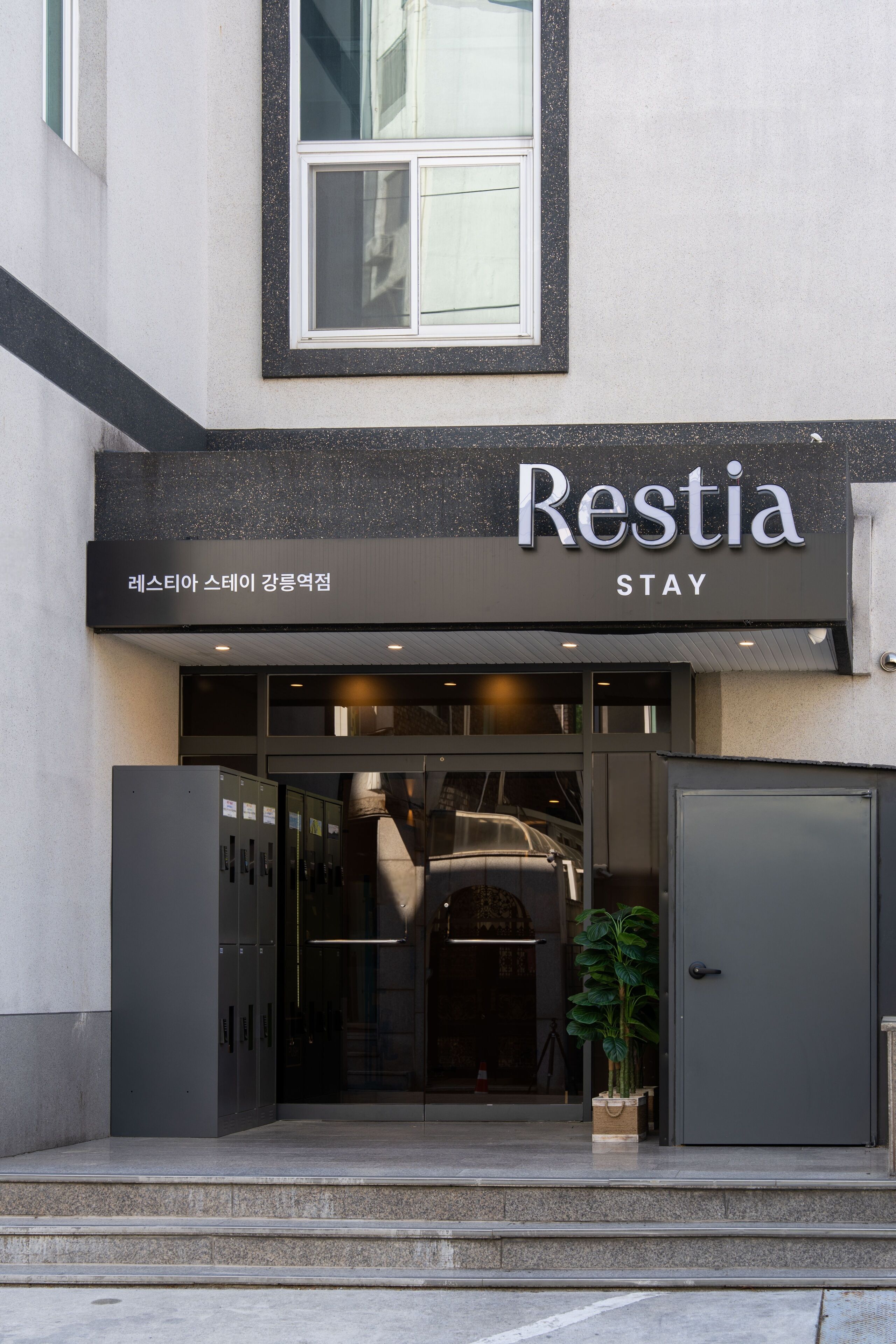 L’entrée d’un immeuble, avec une enseigne indiquant « Restia STAY », et un escalier menant à cette entrée.