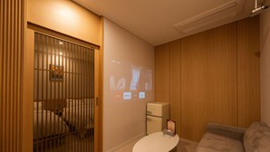 Une pièce moderne équipée d’un écran de projection, d’une petite table blanche, d’un canapé et d’un meuble.