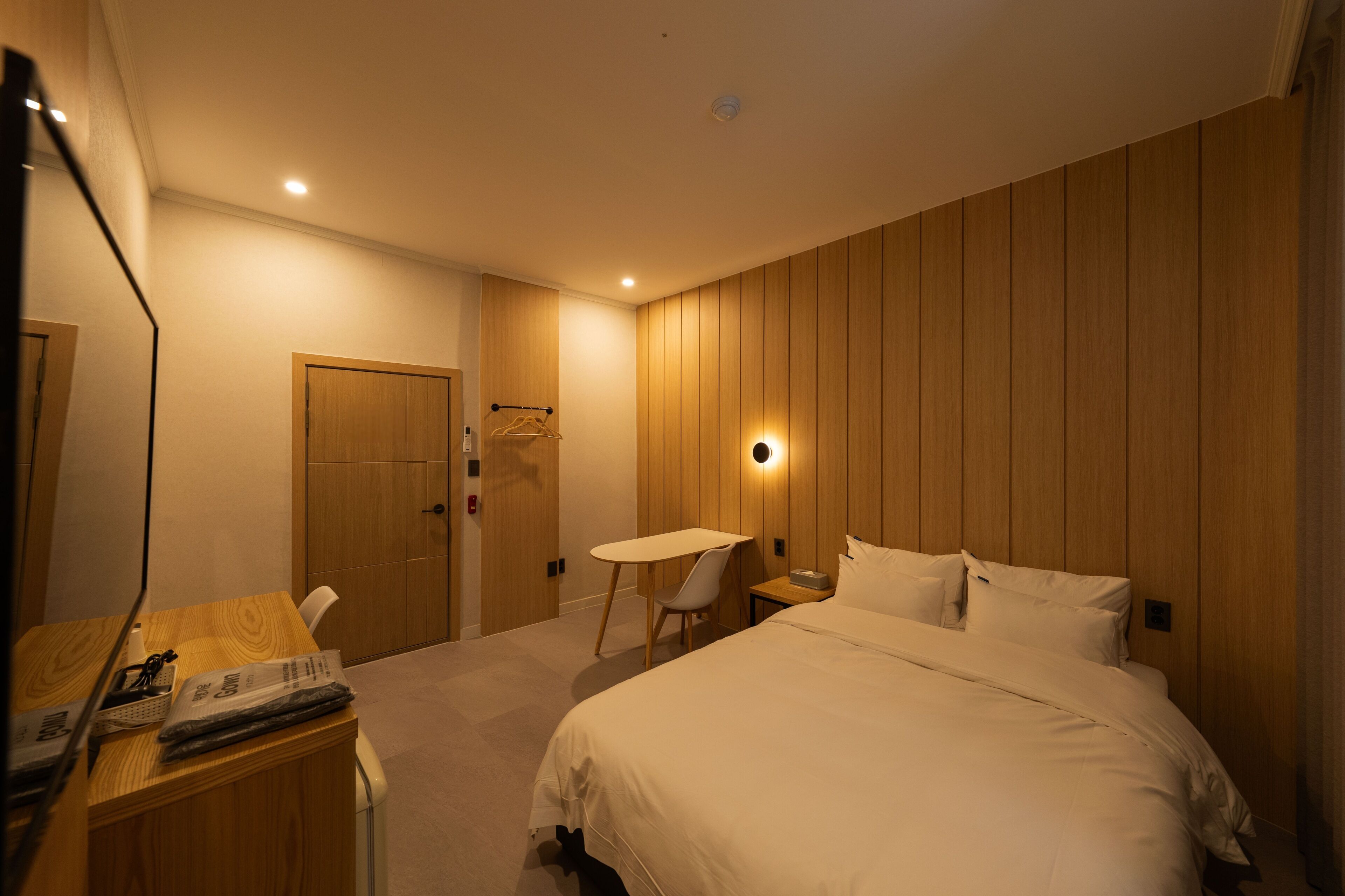 Habitación de hotel con cama, escritorio, silla, mesa y lámpara fijada a la pared.