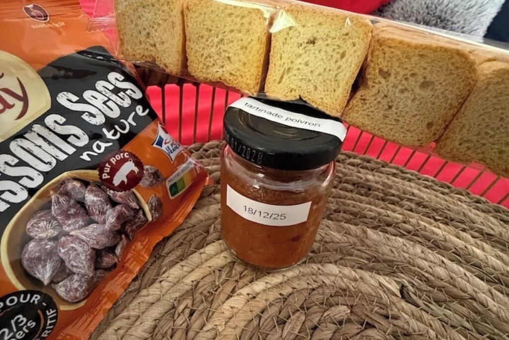 Una confezione di salsicce di maiale 'Sons of the Sun', un vasetto di 'tartrindade polvoron' e diverse fette di pane su un tappetino intrecciato.