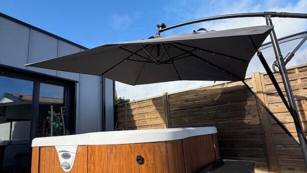 A hot tub with a wooden exterior and a white trim, positioned outdoors with a wooden fence and a modern building in the background.