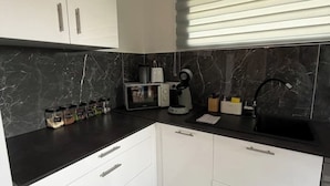 A modern kitchen with white cabinets, a black countertop, and a black marble backsplash.
