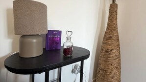 A black table with a textured lamp, a purple book titled 'LE PETIT LIVRE DU RAMBA TRA', and a glass bottle with a heart-shaped stopper.