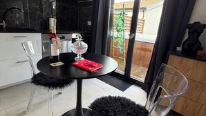 A modern kitchen with a black countertop, a round table with a bottle and a red book, and a glass chair.