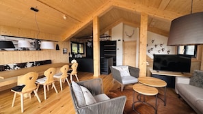 A cozy interior with wooden walls, a dining area with chairs, a sofa, a television, and a kitchen area. - Superior Chalet # 51 with Sauna & Hot Tub (Turrach)