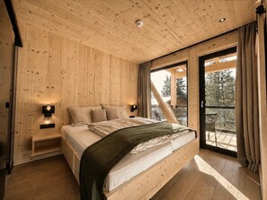 A wooden-paneled bedroom with a bed, bedside lamps, and a view of the outdoors. - Superior Chalet # 50 with Sauna & Hot Tub (Turrach)