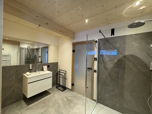 Een moderne badkamer met een douchecabine van glas, een witte wastafel en een grote spiegel.