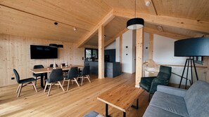 A modern interior with a wooden ceiling, a dining area with a table and chairs, a sofa, and a television mounted on the wall. - Superior Chalet # 53 with Sauna & Hot Tub (Turrach)