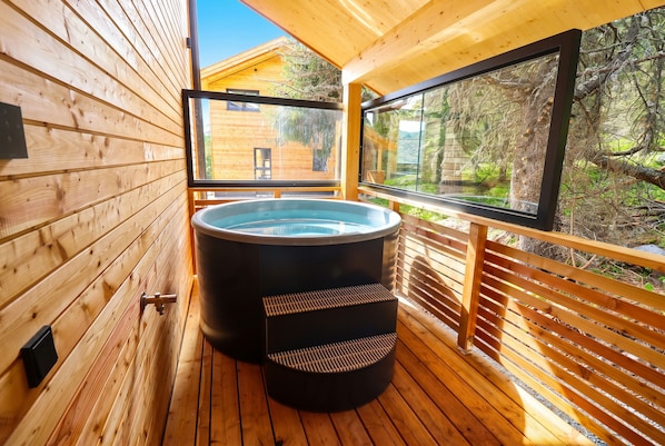 Une terrasse en bois avec un jacuzzi et une grande fenêtre donnant sur une zone boisée.