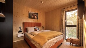 A wooden cabin bedroom with a bed, nightstand, lamp, and a window with curtains.