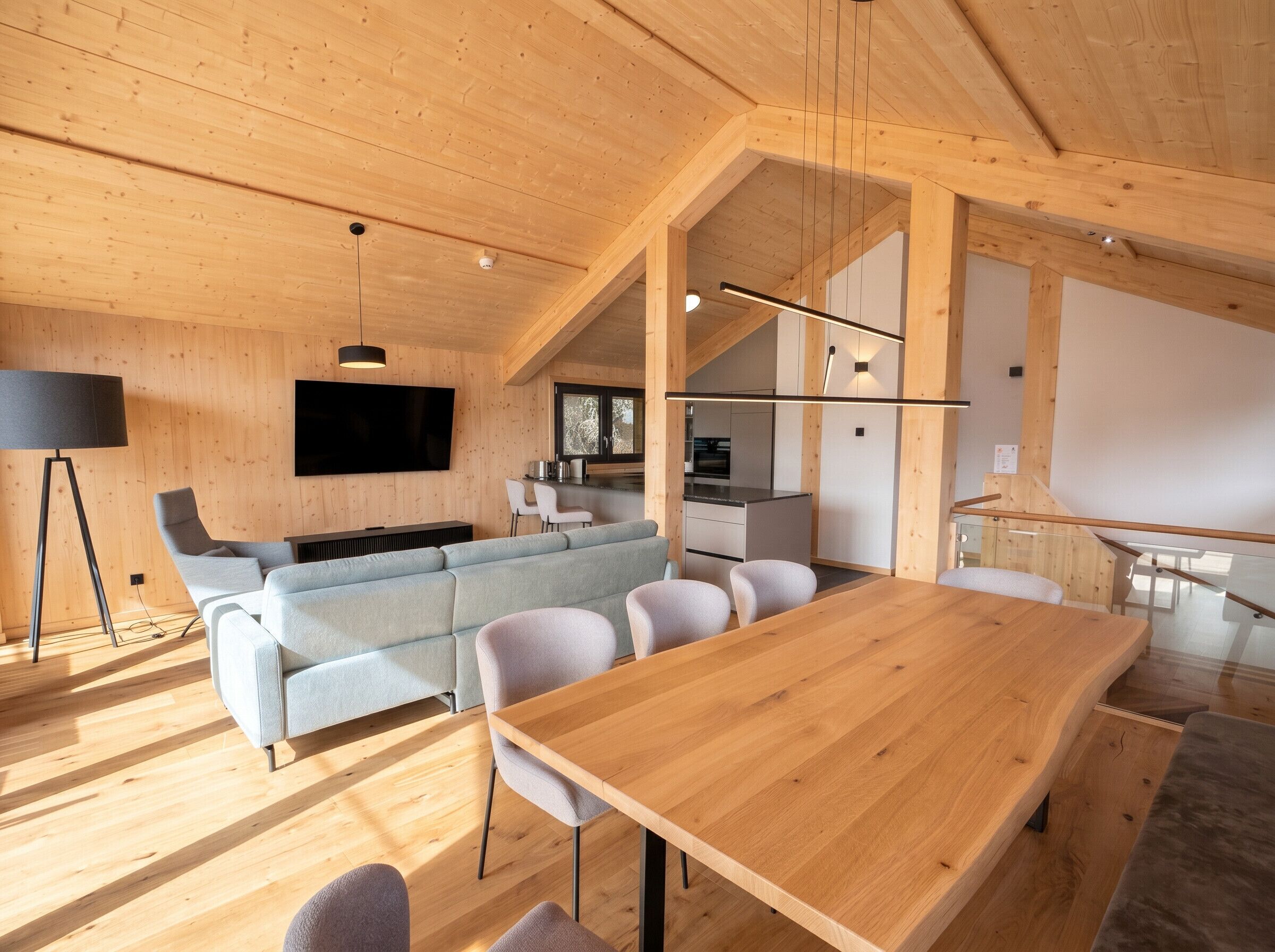 Un intérieur moderne avec un plafond en bois, un ensemble de canapés, une table à manger et un coin cuisine.