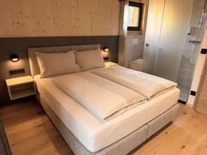 Un lit bien fait dans une chambre dotée d’une tête de lit en bois, d’une petite table de chevet et d’un luminaire fixé au mur.