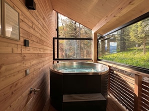 A wooden cabin interior with a hot tub, wooden walls, and a large window overlooking a forest. - Superior Chalet # 55 with Sauna & Hot Tub (Turrach)