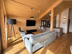 A modern interior with a wooden ceiling, a sofa, a TV, and a kitchen area. - Superior Chalet # 55 with Sauna & Hot Tub (Turrach)