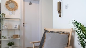 A room with a wooden chair, a shelf with decorative items, a door with a Wi-Fi sign, and a wall-mounted telephone. - Orchid Cozy Studio & Balcony in Larnaca (Larnaca)
