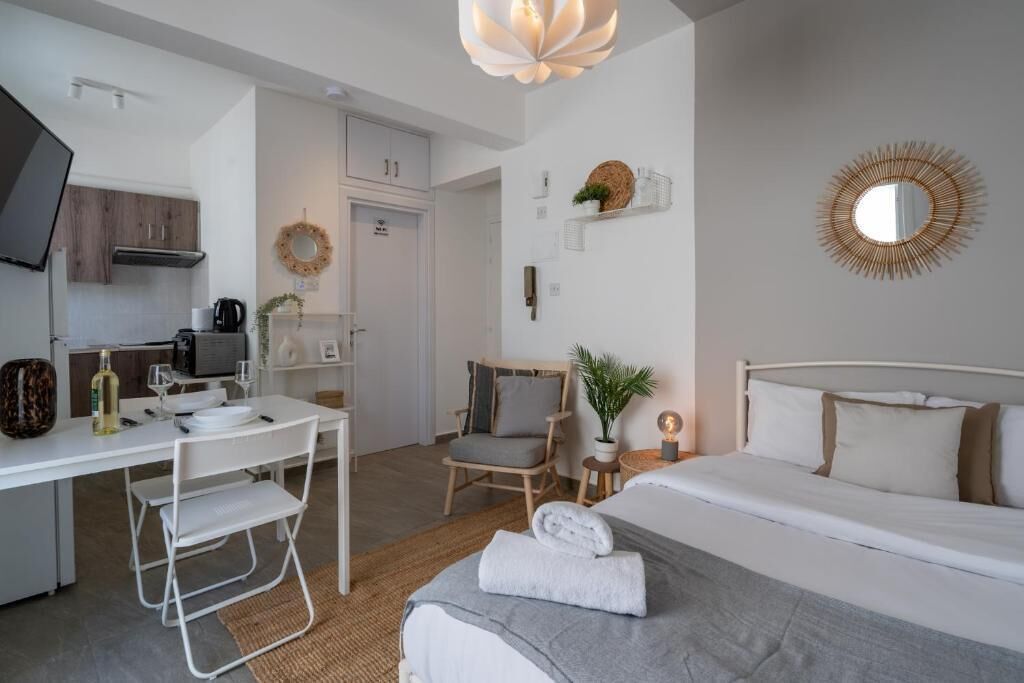A modern hotel room with a bed, a desk with a chair, a TV, and a small table with a plant.