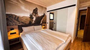 Ein modernes Schlafzimmer mit einem großen Bett, einem Nachttisch, einem wandmontierten Spiegel und einem Wandgemälde von einem Berg.