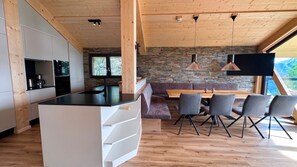 Eine moderne Küche mit einer zentralen Kochinsel, einem Essbereich mit Holztisch und Stühlen sowie einer Steinwand im Hintergrund.