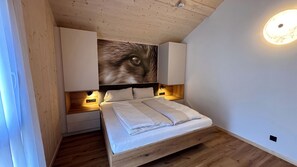 Une chambre à coucher avec un lit en bois, une tête de lit ornée d’un motif représentant une tête de loup, des lampes de chevet et un luminaire fixé au mur.