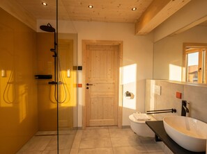 Une salle de bain moderne avec une douche à parois de verre, une porte en bois, des toilettes, un lavabo avec un meuble-vasque et un miroir.