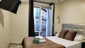 Ein Hotelzimmer mit Bett, Wandfernseher, Fenster mit Blick auf Gebäude und einer Tür.