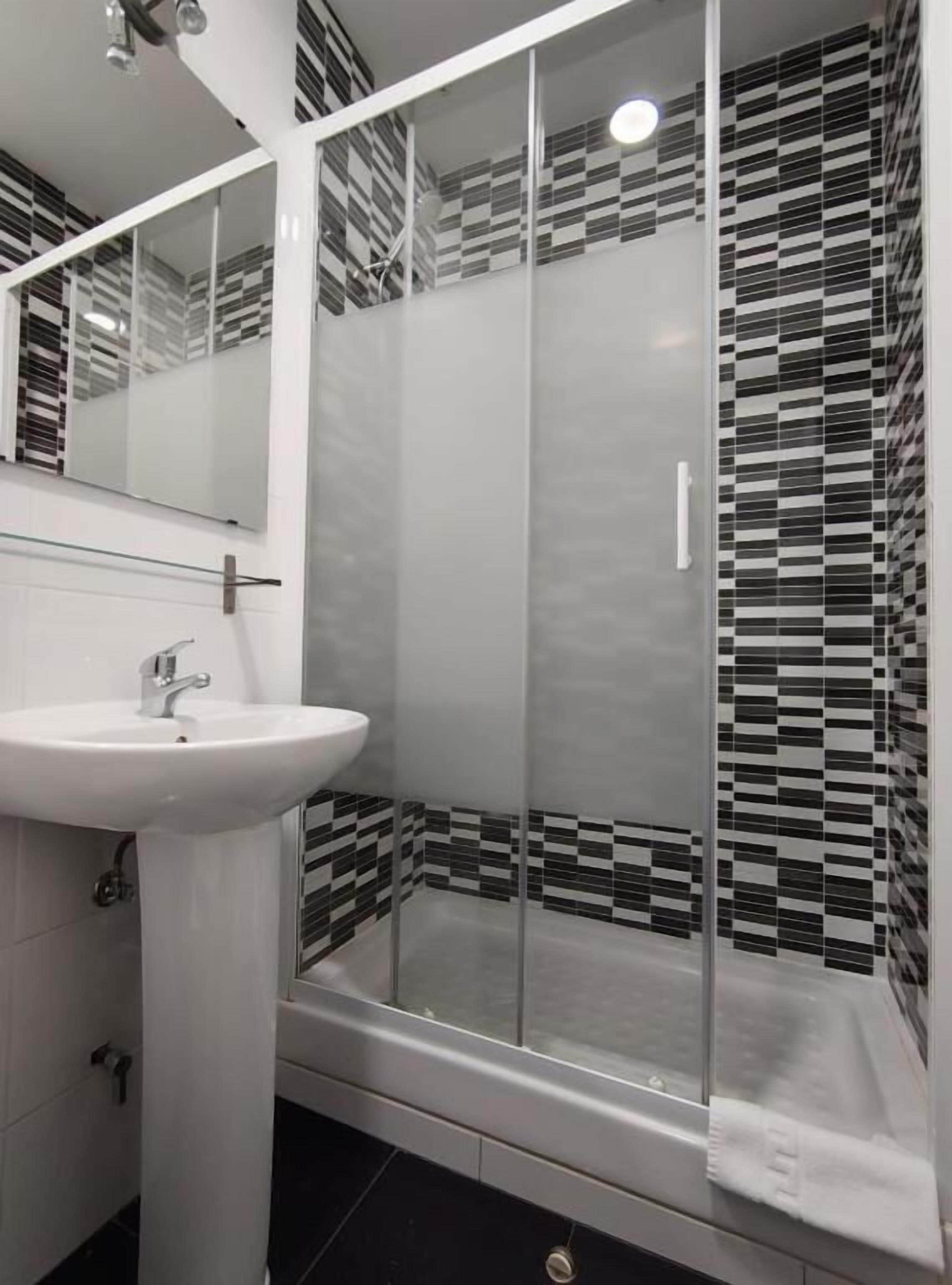 A modern bathroom with a glass-enclosed shower, a white sink, and a mirror above it.