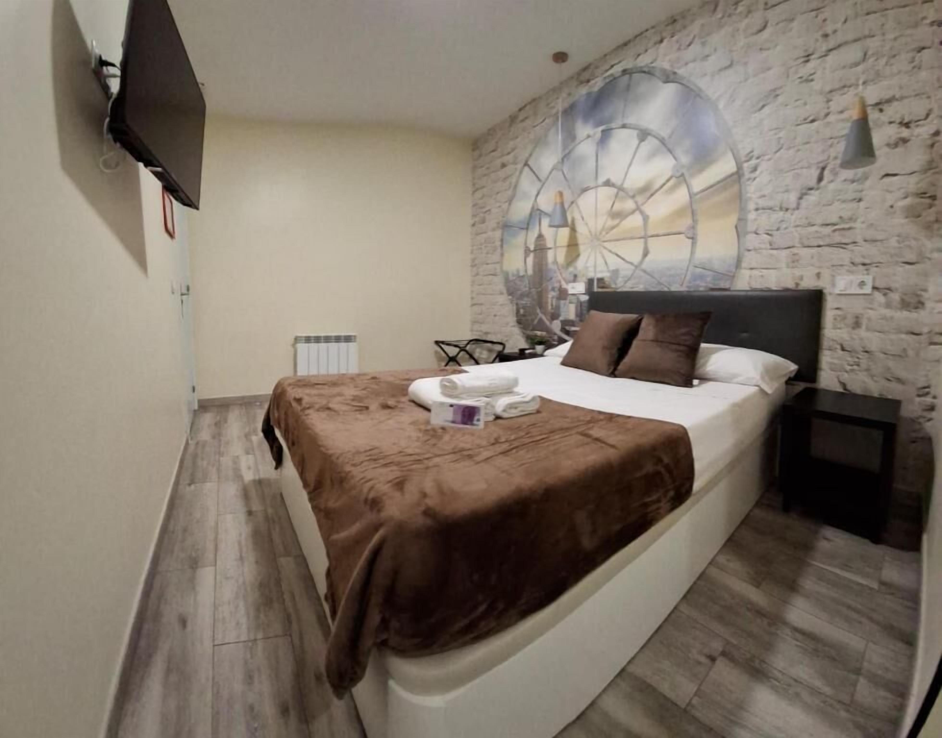 A bedroom with a bed, a wall-mounted TV, a large circular mural, and a wooden floor.