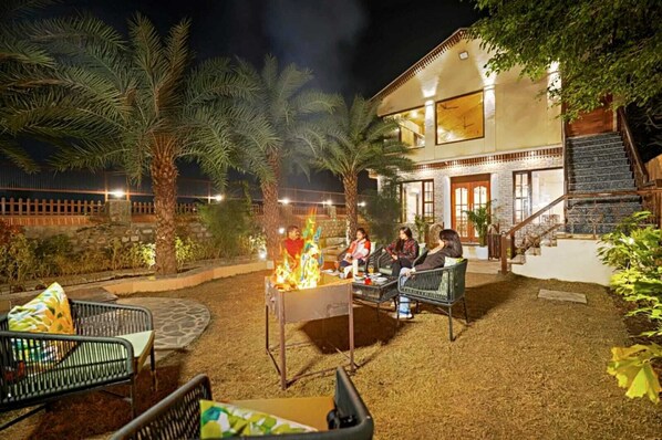 An outdoor seating area with a fire feature, surrounded by palm trees and a stone wall.