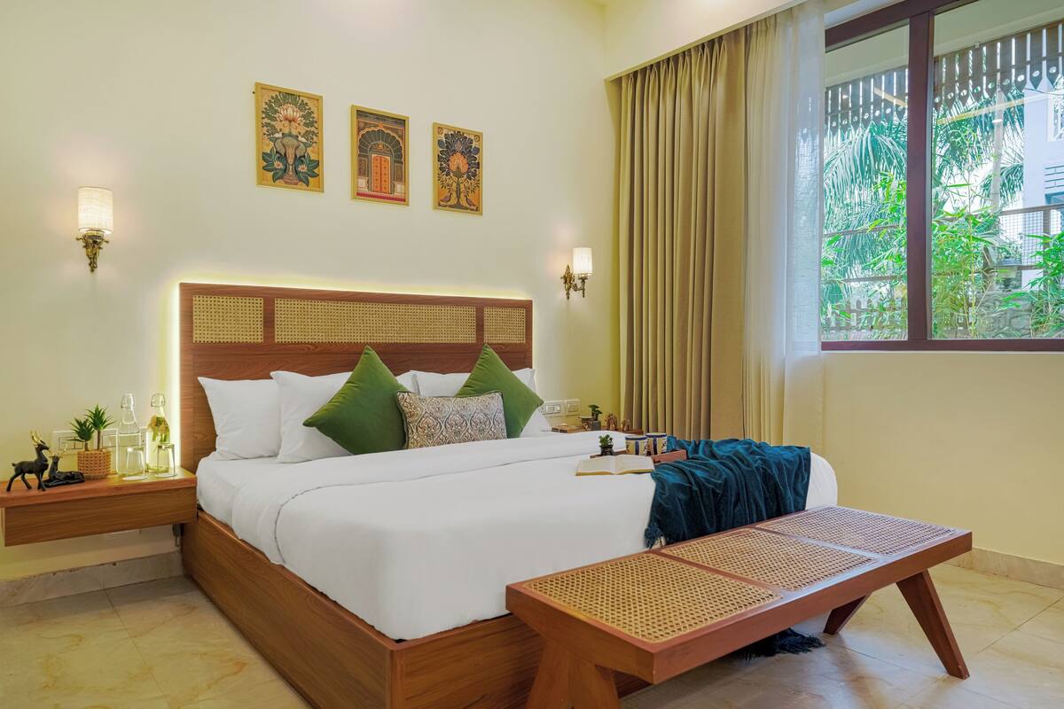 A neatly arranged hotel room with a bed, bedside tables, a bench, and a window with curtains.