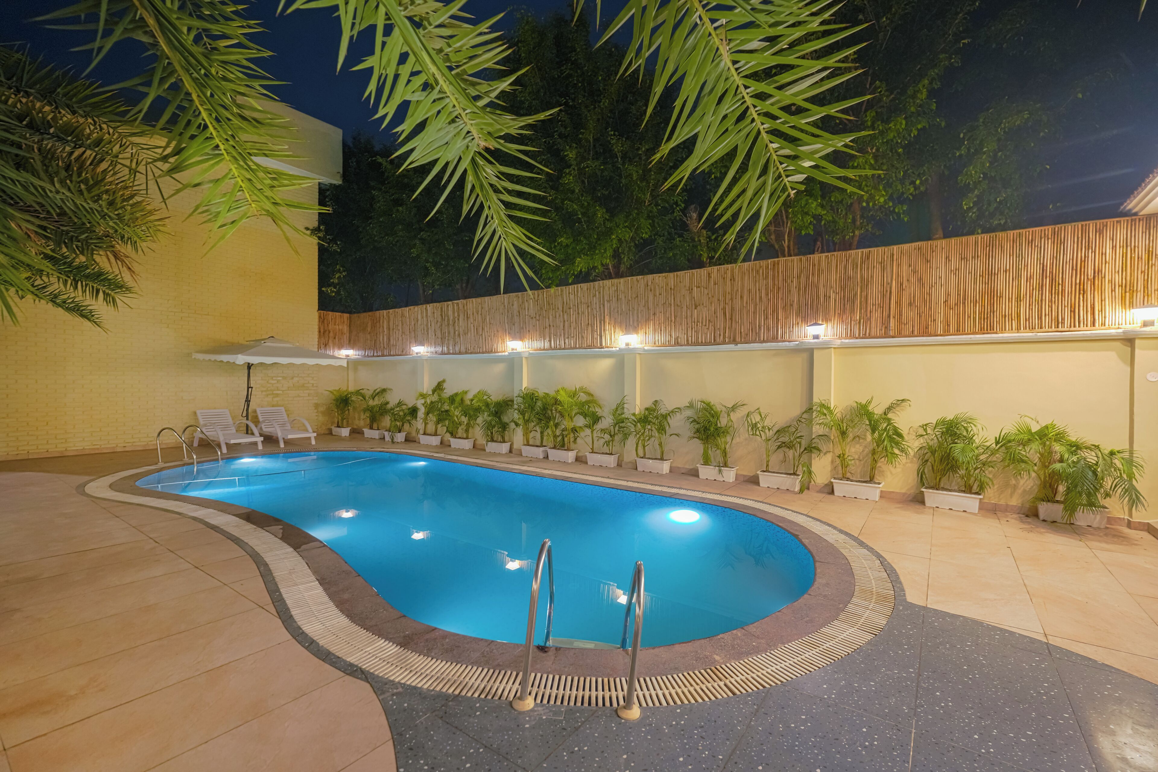 An indoor swimming pool with a tiled floor, surrounded by potted plants and a bamboo wall.