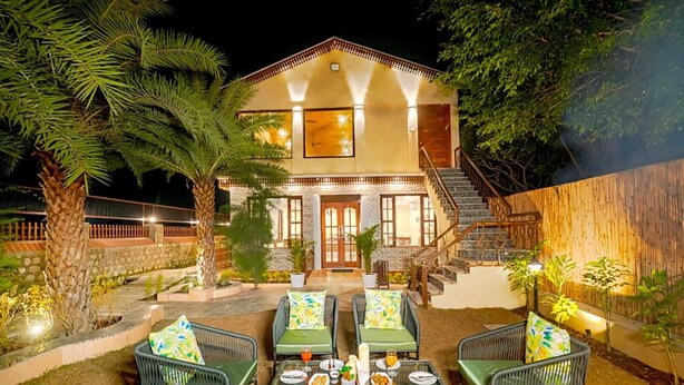 A two-story house with a stone facade, a wooden staircase, and outdoor seating with a table set for dining. - Manovan Resort by Eastlynn Experiences, Jim Corbett (Kaladhungi)