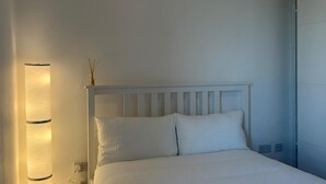 Ein Schlafzimmer mit einem weißen Bett, einem weißen Kopfteil und einem Nachttisch mit einer Lampe.